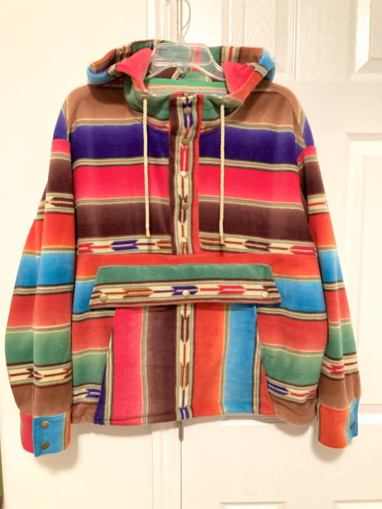 a bright multicolor hooded pullover made of fleece hanging against a white wall