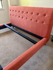 Image of a coral upholstered headboard and frame pulled apart in a carpeted room.