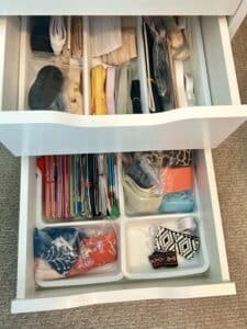Two desk drawers pulled out to see the organizers inside. In the top drawer are neat bundles of lingerie elastic. The bottom drawer holds bias tape cards organized by color.