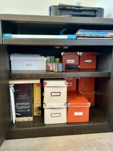 A dark wood cupboard with the doors open. Inside are white an orange boxes stacked neatly. Everything is precise and tidy.