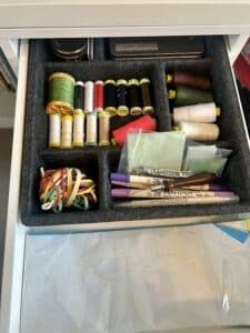 the inside of a desk drawer with a desk organizer in it. There are spools of thread, pens, and post it notes put neatly into the organizer compartmetns.