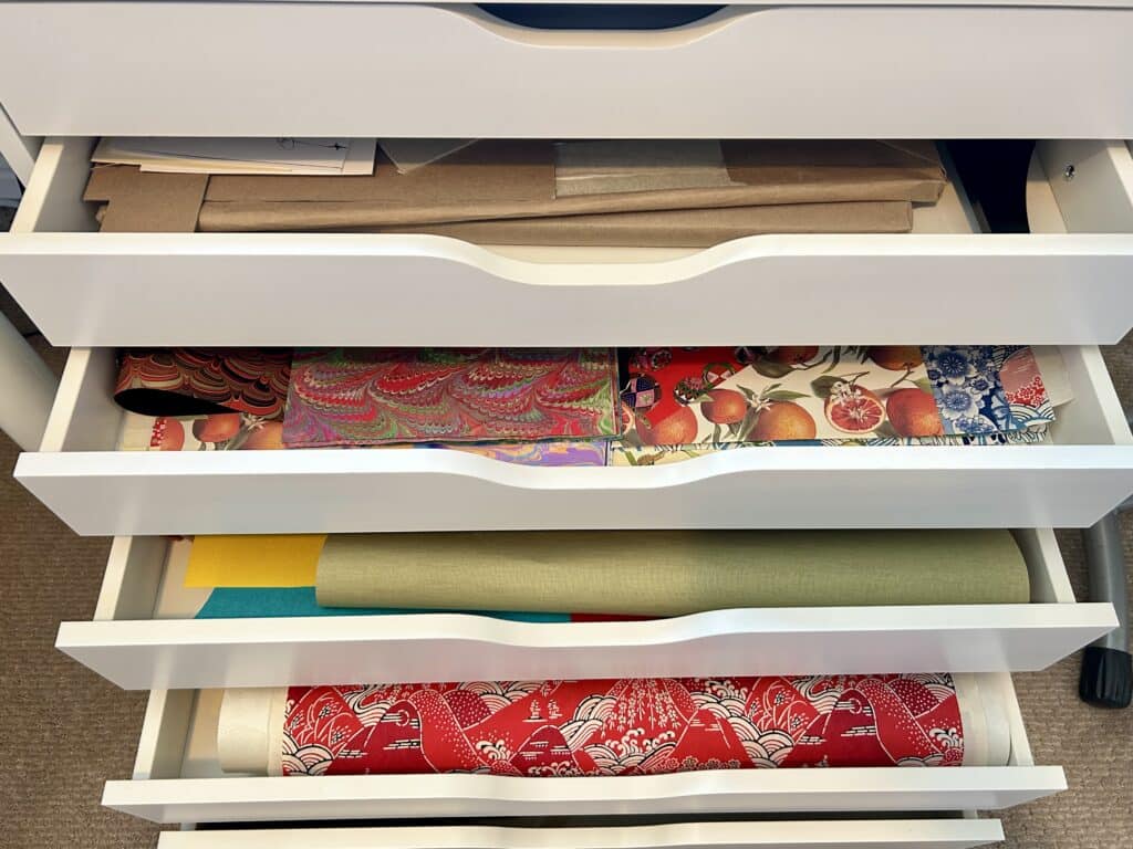 Closeup of a chest of drawers with the drawers somewhat pulled out. You can see mat board and decorative patterned paper in the drawers. 