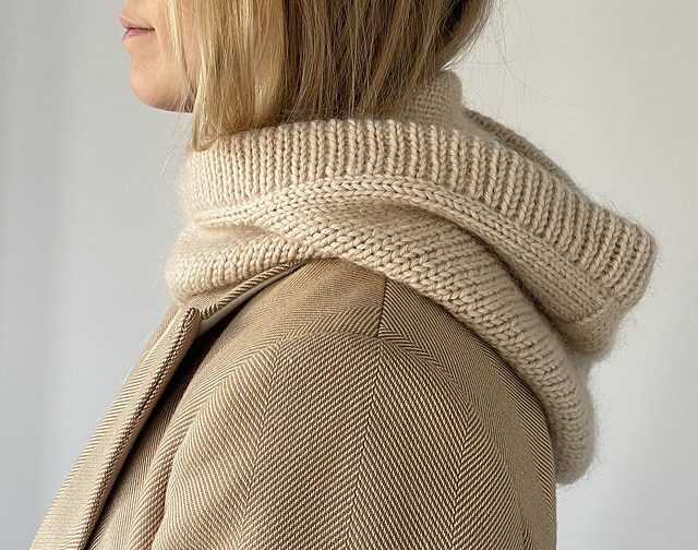 The same beige knitted hood being warn pushed back on top of a coat. 