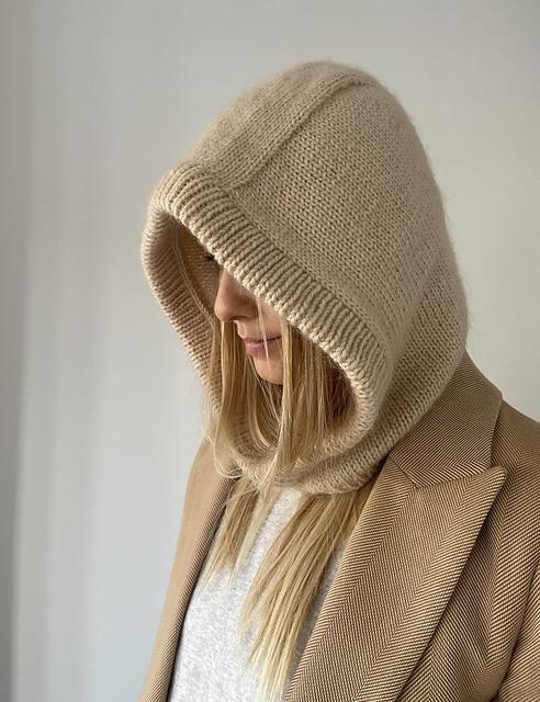 Pattern photo of a beige knitted hood pulled up around a blonde woman's face. 