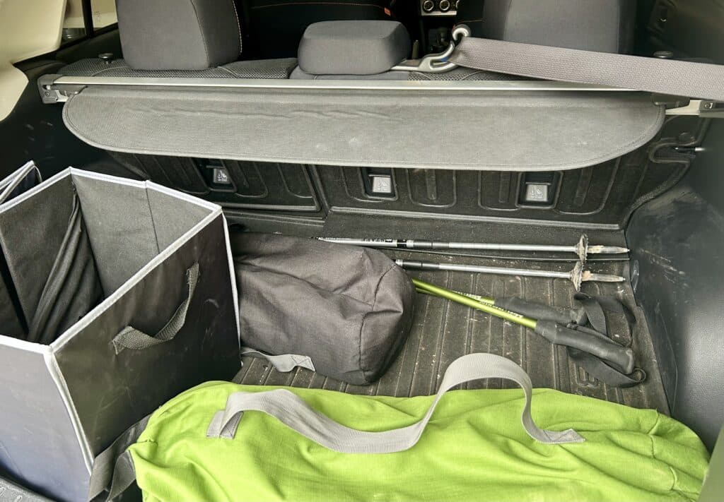 The back of a car with trekking poles, camp chairs, and a bin messily strewn around. 