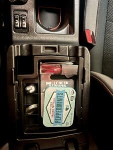 A top tray in a car's center console. There are mints and lip gloss and a canyon pass neatly arranged in it.