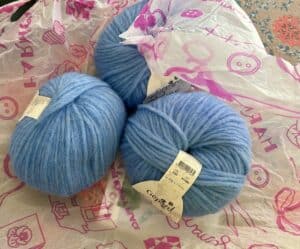 Three balls of chunky sky blue yarn sit in a pile on the tissue they shipped in.