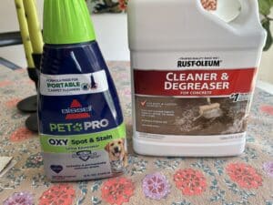 A bottle of "Urine Eliminator" carpet cleaner and a bottle of garage cleaner and degreaser sit on a kitchen table