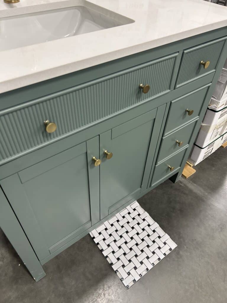 A green bathroom vanity in a showroom with a black and white tile sample near it