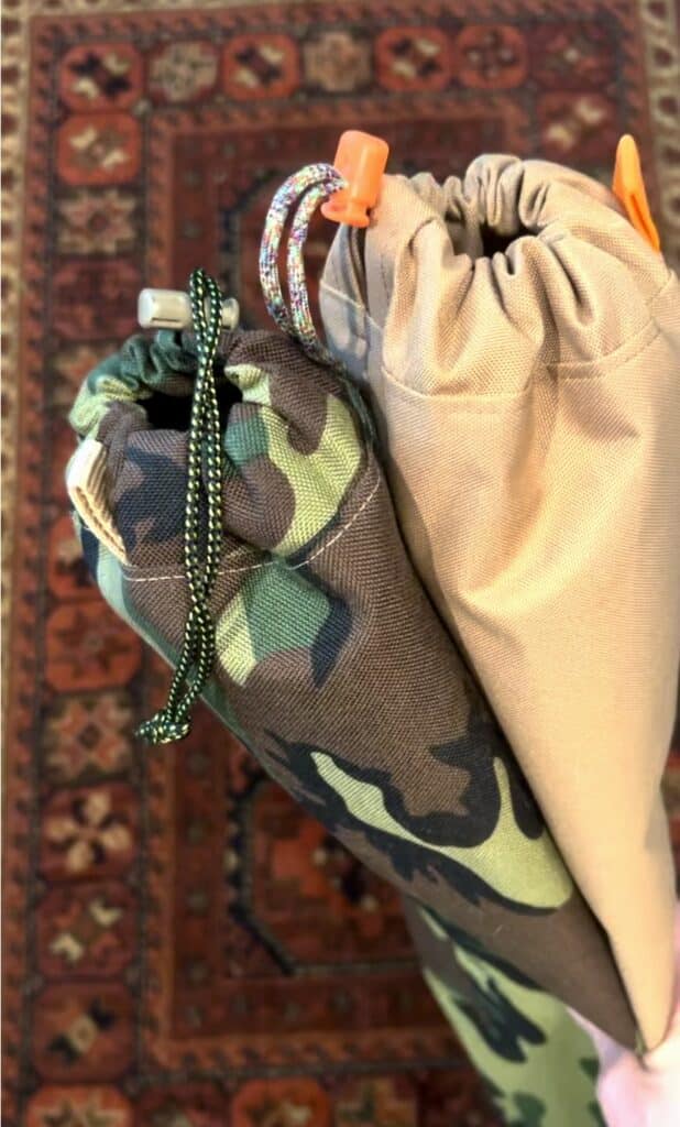 Two stuff sacks for trekking poles. One is camo print and one is tan with an orange cord lock.