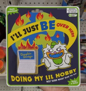 A fake toy with packaging that reads, "I'LL JUSTBE OVER HERE DOING MY LIL HOBBY NOT SURE WHAT ELSE TO DO Helps a little!"