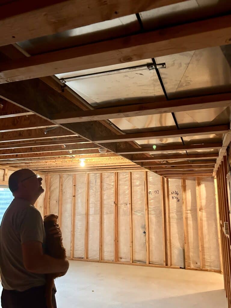 A man holding a cat looks up at the ducting that has been framed in 