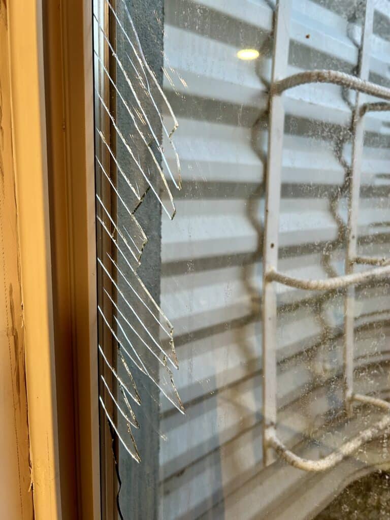 Closeup of a double-paned basement window. The inside pane is broken. 