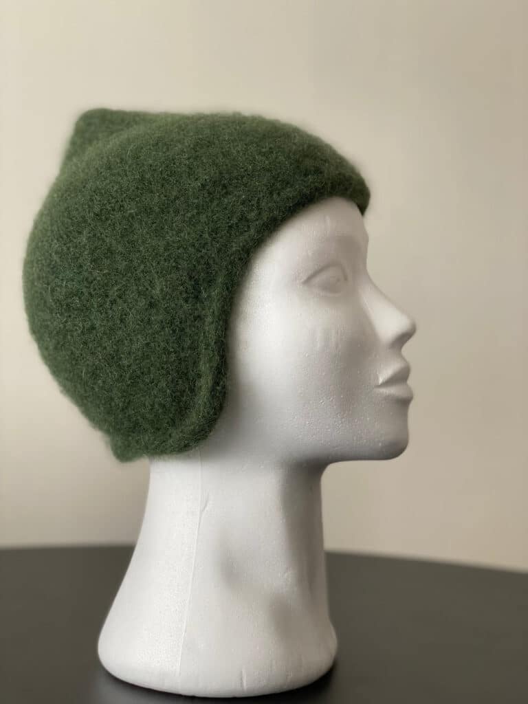 A green felted hat with short fitted earflaps is displayed on a mannequin head