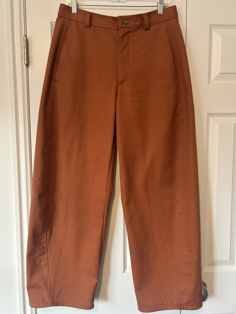 A pair of sienna brown barrel leg trousers hanging on a white closet door