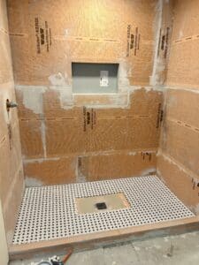 A shower stall that's ready to be tiled. There is black and white mosaic tile on some of the floor