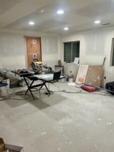 A drywalled basement with a deluxe tile saw set up and lots of gear scattered around