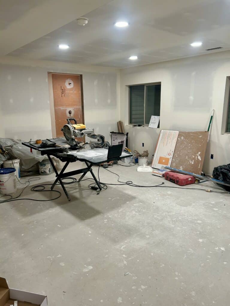 A drywalled basement with a deluxe tile saw set up and lots of gear scattered around
