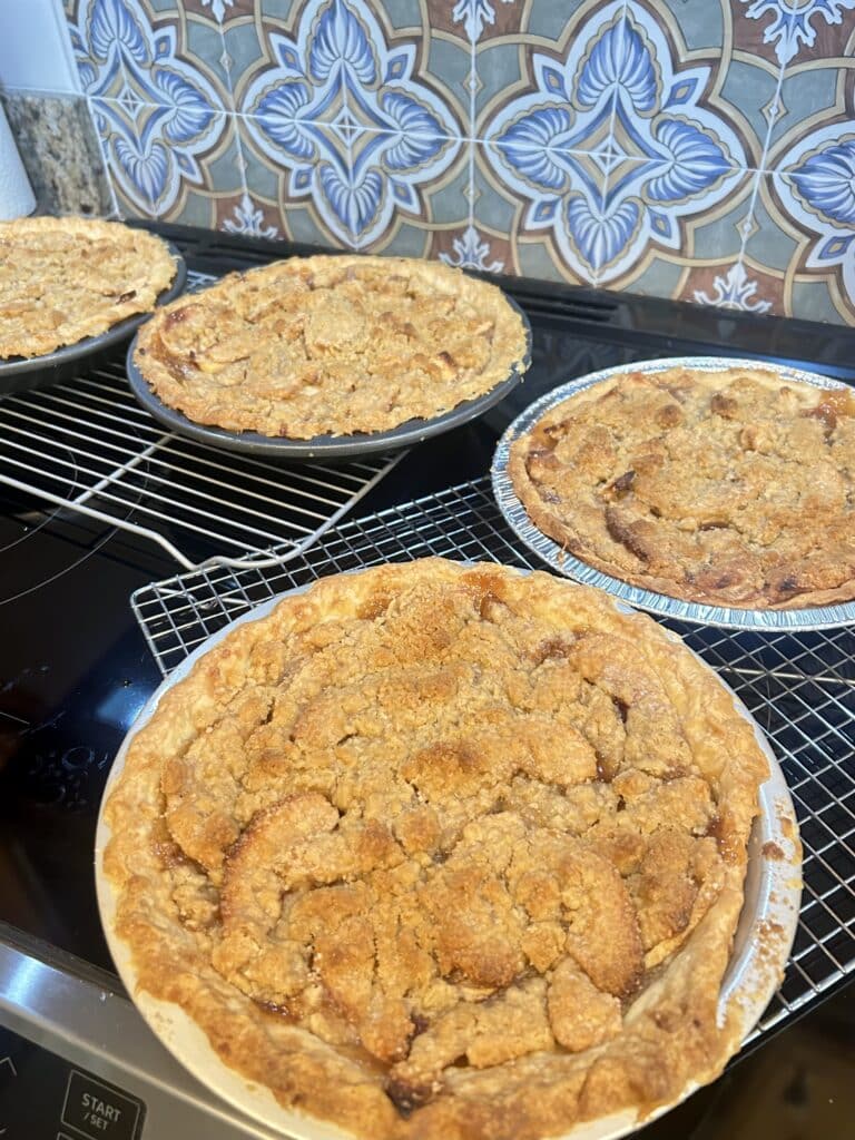Four apple pies with a crumb top crust sit on a stove top