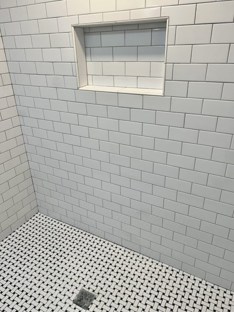 A shower enclosure with white subway tiles on the wall and black and white mosaic tile on the floor 