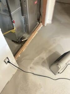 Closeup of a space heater on a raw concrete floor in a basement, near a utility room.