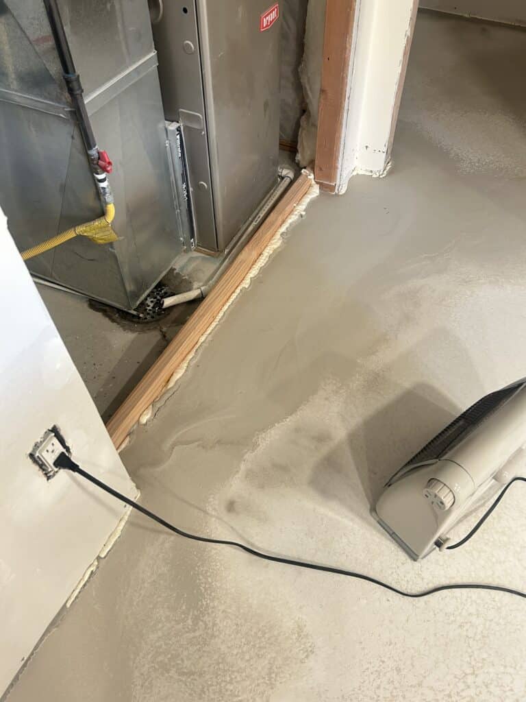 Closeup of a space heater on a raw concrete floor in a basement, near a utility room.