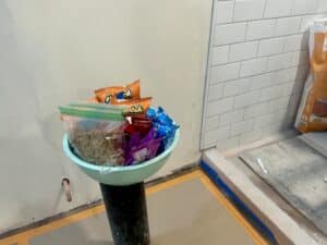 A bowl of chips and snacks sits on top of the stand pipe for the toilet in a bathroom.