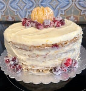 A layer cake with white frosting and decorations of cranberries and a mandarin orange