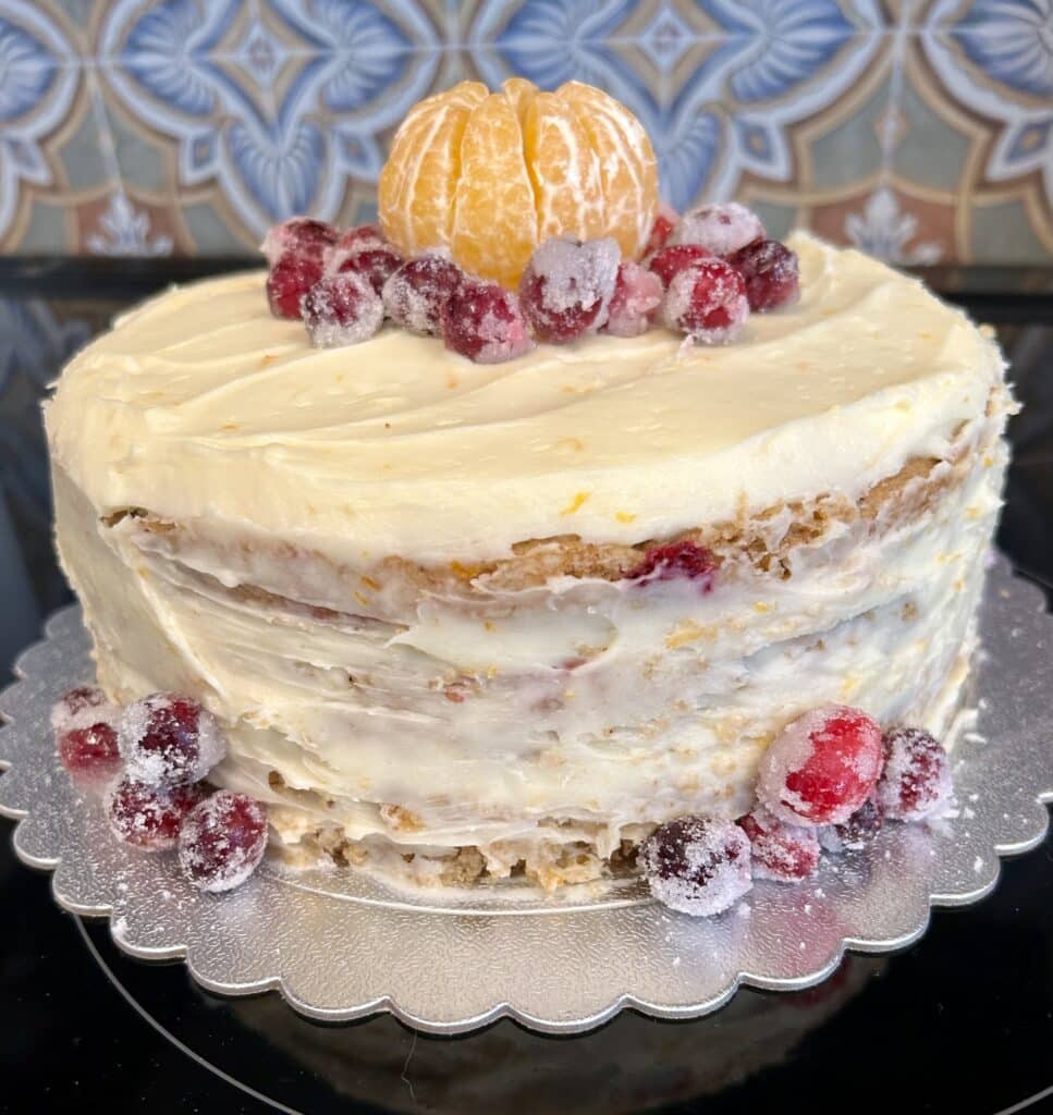 A layer cake with white frosting and decorations of cranberries and a mandarin orange