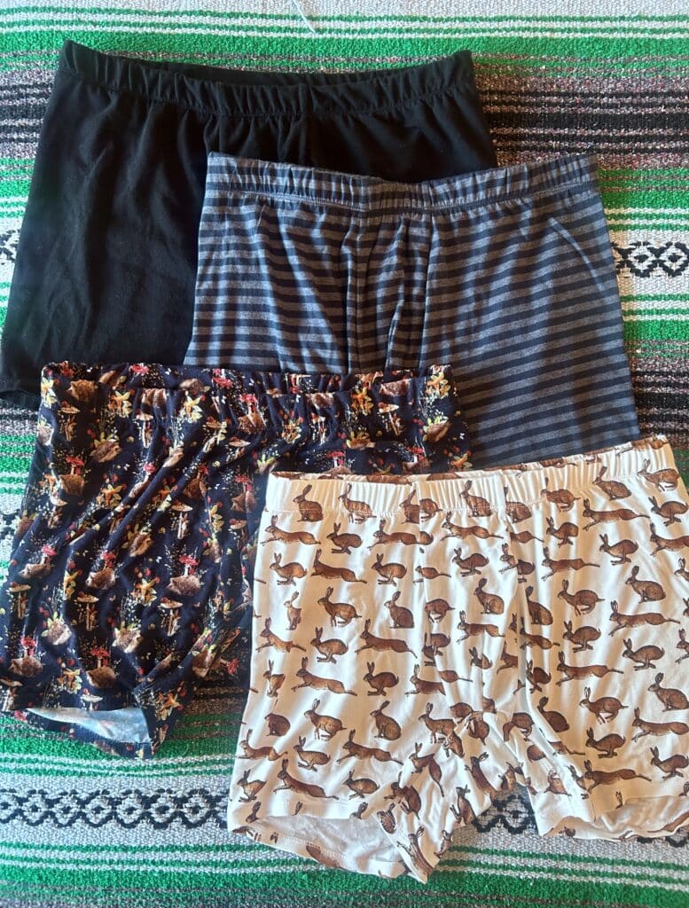 Four pairs of men's underwear laid out on a bed. One is black, one is striped in gray and black, one has hedgehogs and mushrooms on a black background, and one has brown rabbits on a white background.