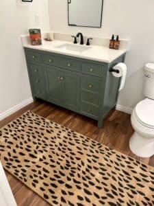 A bathroom with a green vanity, a leopard rug, and white walls