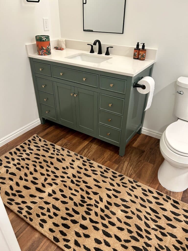 A bathroom with a green vanity, a leopard rug, and white walls 