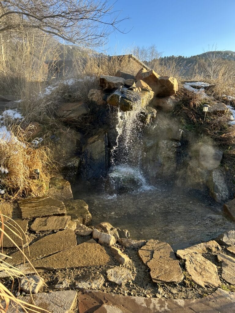 A stone pool with a waterfall, steaming in the winter afternoon 