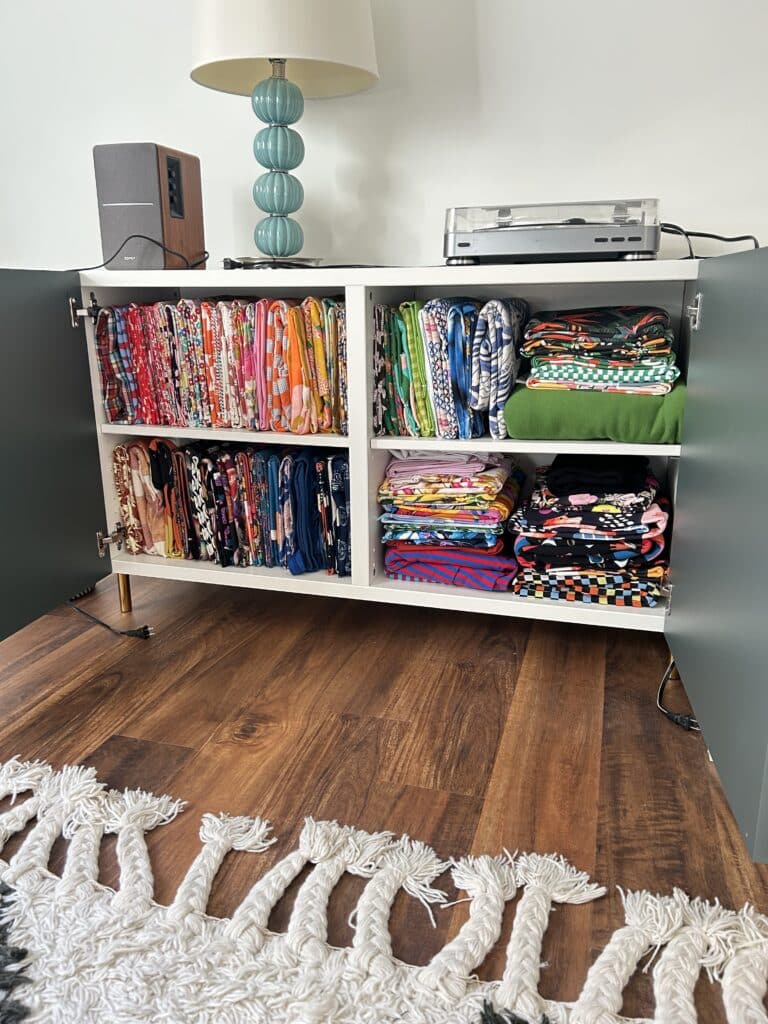 A cabinet with green doors stands open. It is filled with folded fabric. 