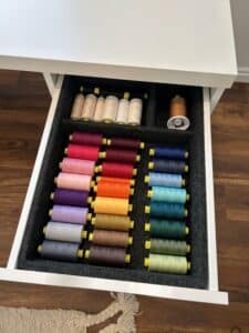 A desk drawer is pulled out. It's filled with thread in rainbow order.