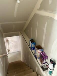 An unfinished stairwell leading into the basement. Various pantry items are stacked on the stair ledge.
