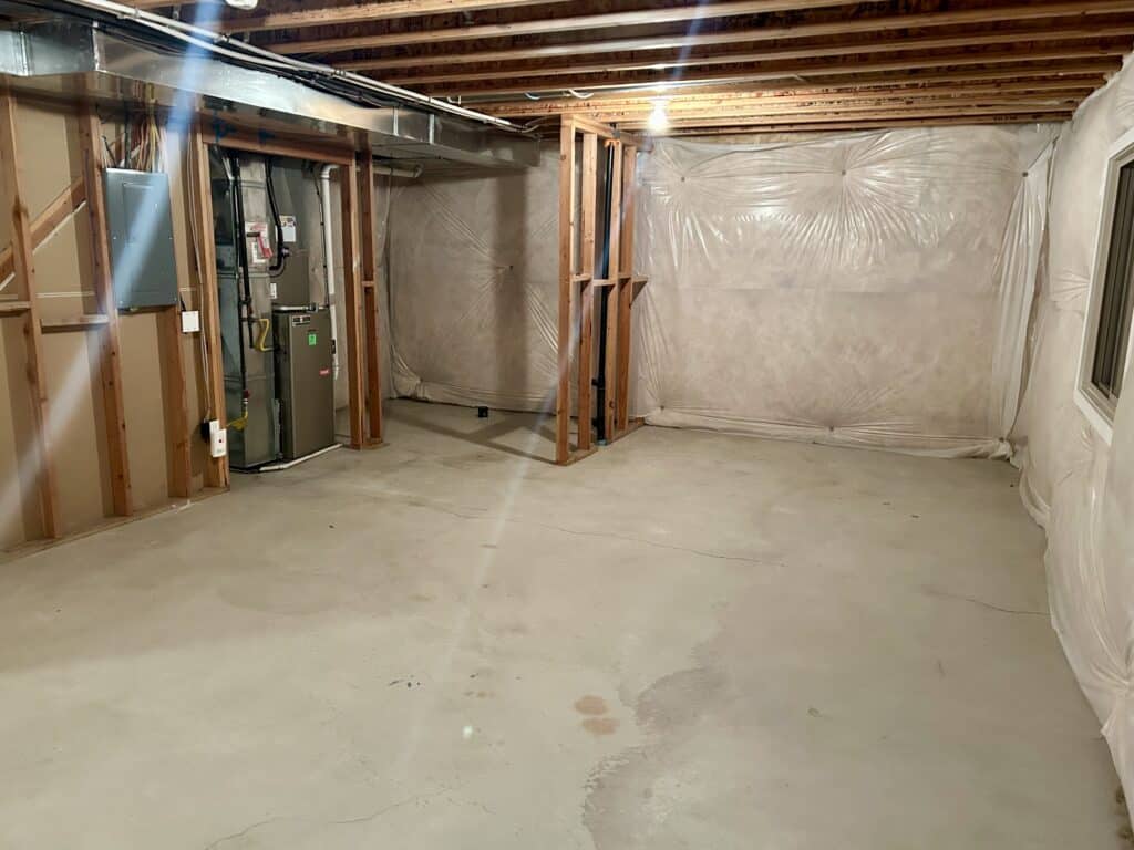 An unfinished basement from the corner of the room. The insulation and furnace are exposed. 