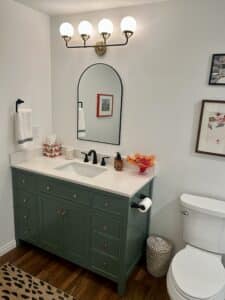 A green bathroom vanity with the tissue box cover and a piece of orange art glass on it.