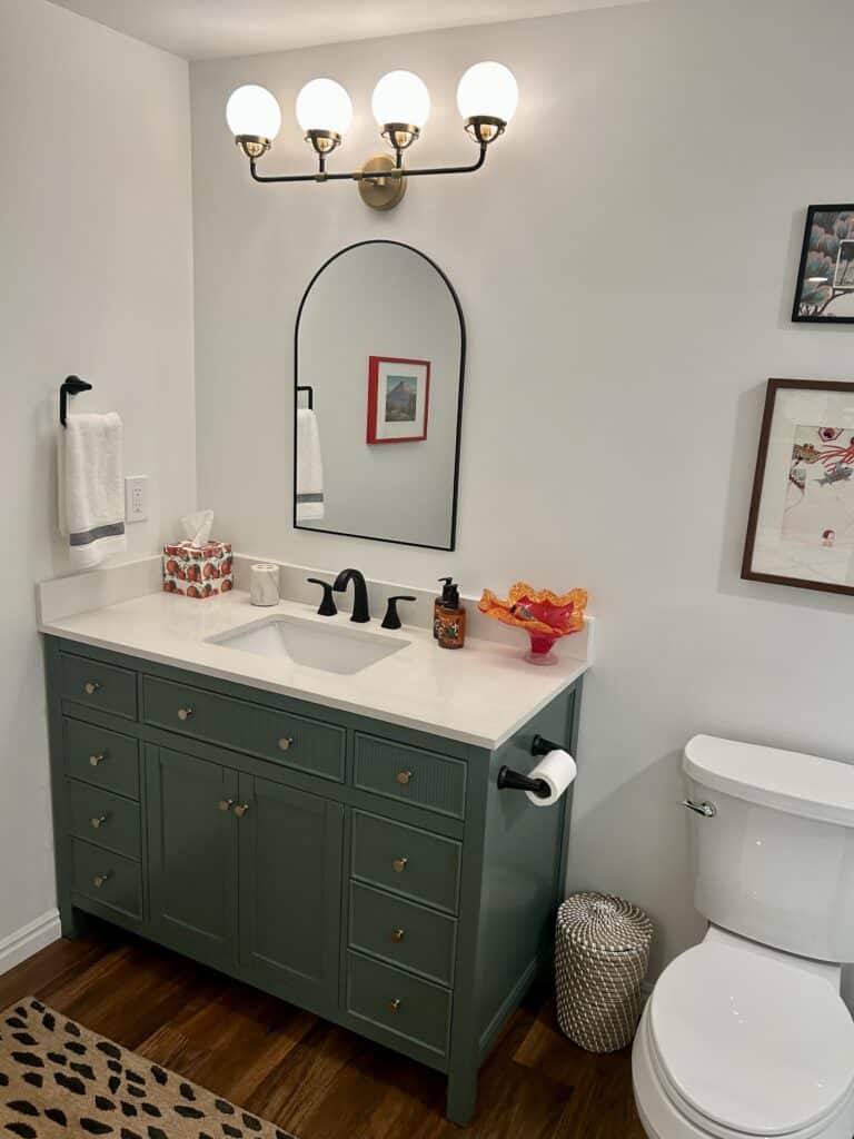 A green bathroom vanity with the tissue box cover and a piece of orange art glass on it. 