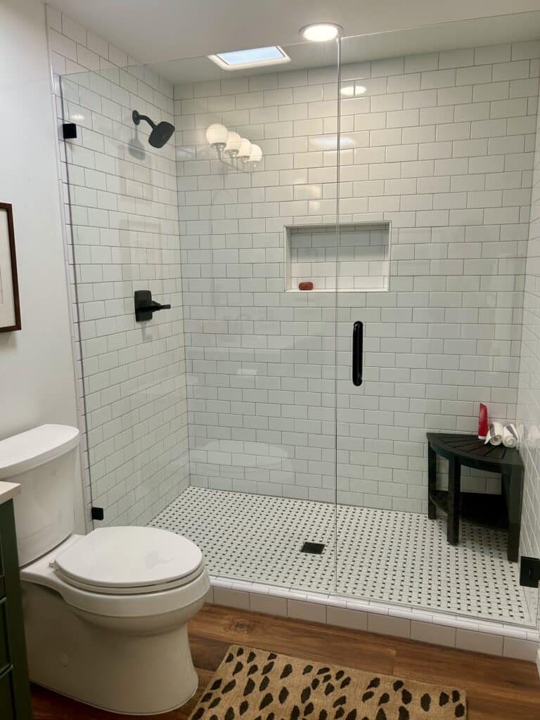 A tiled shower with a black stool in it and a solid glass door
