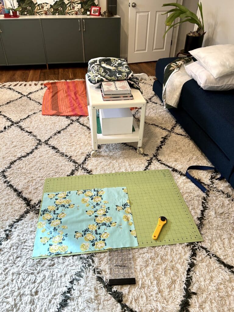 A white fluffy rug has a cutting mat, pieces of fabric, and pillow forms on it.
