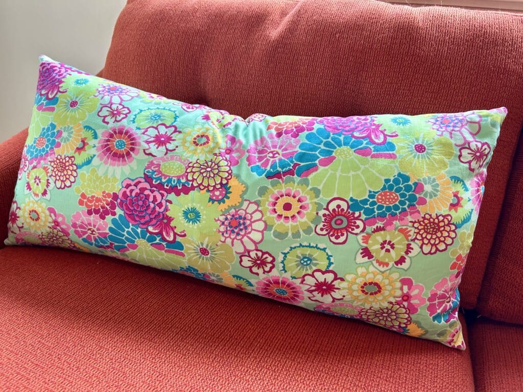 A long narrow pillow in aqua japanese print on an orange couch