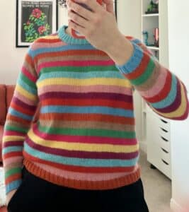 A mirror selfie of a woman in a rainbow striped sweater