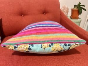 Closeup of the zipper at the bottom of a rainbow striped knit pillow.