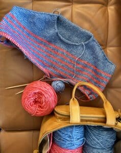 A blue sweater with red stripes being knitting. Just the yoke of the sweater is finished.