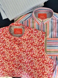 Two shirts being sewn with collars but no sleeves. One is small pink floral and one is blue and purple stripes.