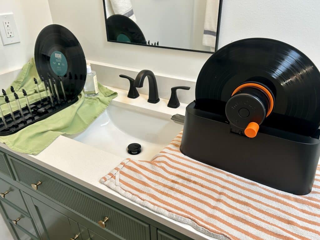 A spinning record cleaner and a drying rack on either side of a bathroom sink