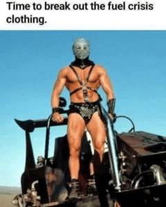 Screenshot from a Mad Max movie with a man in a harness and leather shorts strapped to the front of a car. Text says, Time to break out the fuel crisis clothing.
