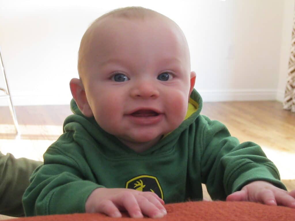 A baby looks over the edge of a couch and smiles