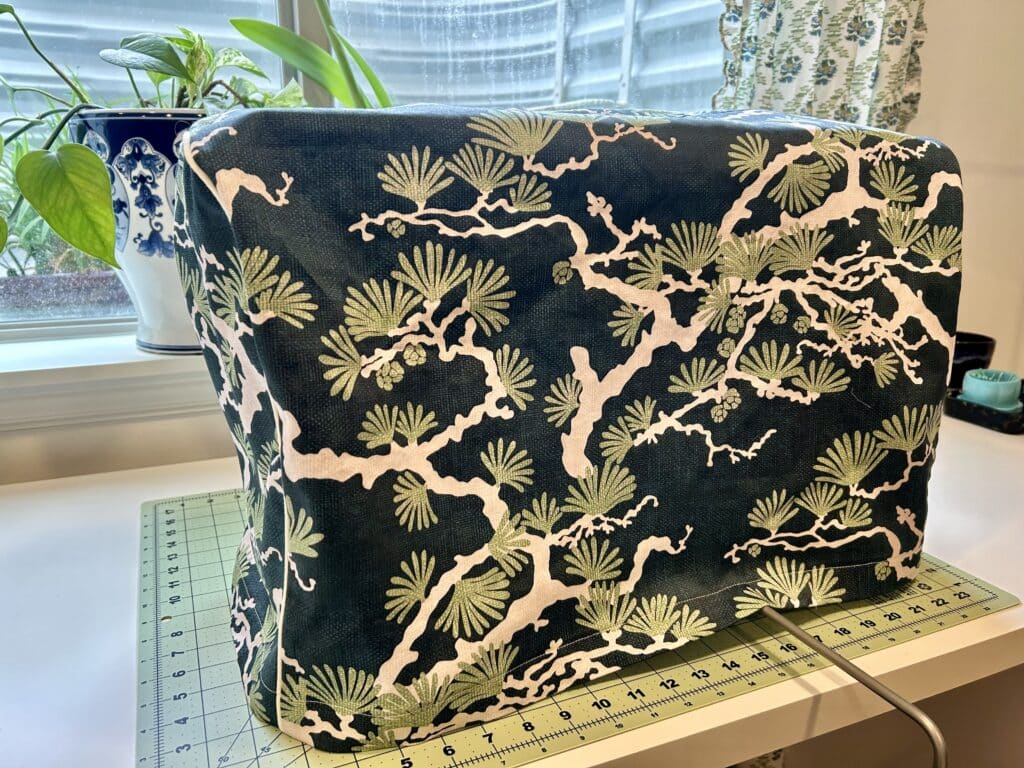 A sewing machine with a cover on it. The cover has a print of a Japanese pine tree in white and green on a dark teal background.